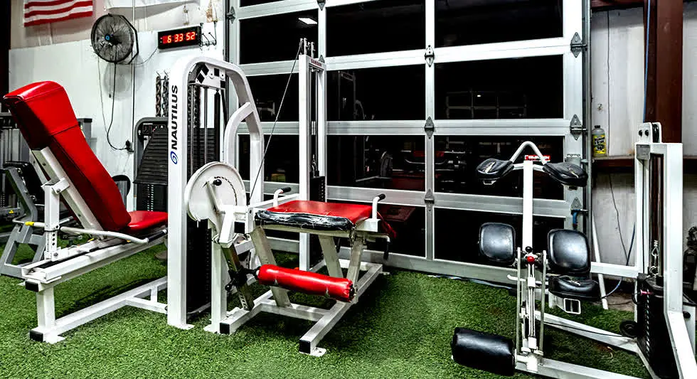 The machine floor: rows of plate-loaded and selectorised machines on turf, lit by the roll-up doors.